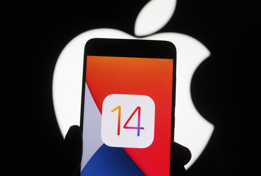 In this photo illustration the iOS 14 logo of the iOS mobile operating system is seen displayed on a mobile phone with an Apple logo in the background.