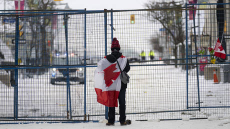 A lone protester stands draped in the Canadian flag at a temporary fence controlling access to streets near Parliament, in Ottawa, February 20, 2022.